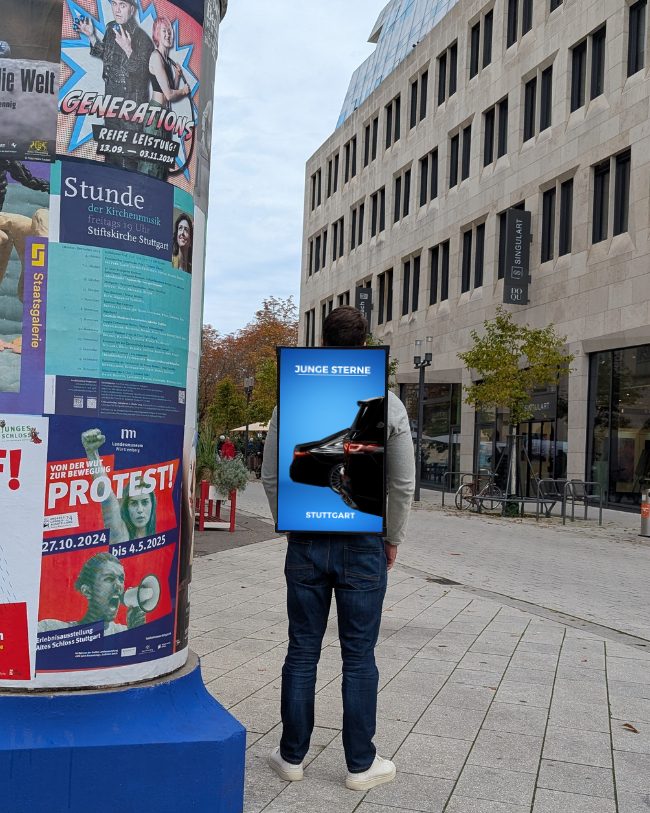 WalkingScreen neben einer klassischen Litfaßsäule mit Papierplakaten